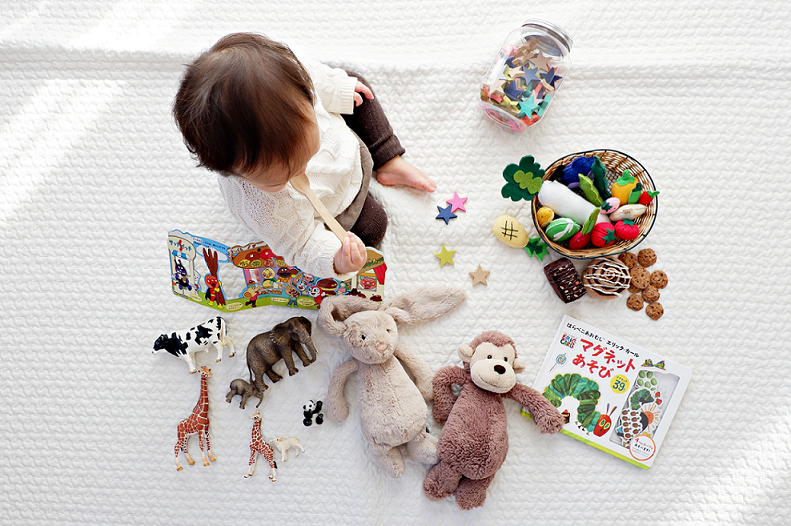 Toddler sitting on blanket surrounded by toys